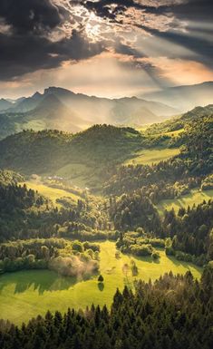 the sun shines brightly through the clouds over green hills and valleys in the mountains