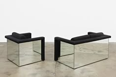 two black chairs sitting next to each other on top of a cement floor in front of a white wall