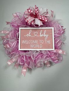 a pink and white welcome sign hanging on the side of a wall with ribbon around it