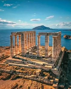 an ancient greek temple overlooking the ocean with mountains in the backgrouds and blue sky