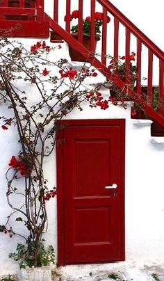 a red door is next to a white building with flowers growing on the outside wall