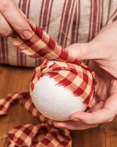 a person holding a white ball with red and tan plaid ribbon around it on top of a wooden floor