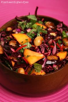 a wooden bowl filled with salad on top of a pink plate