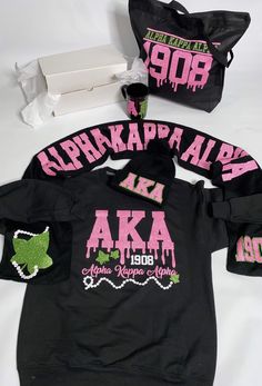 two black shirts with pink and green designs on them, one has a bag next to it