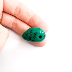 a hand holding a small green object with writing on it's thumb and fingers