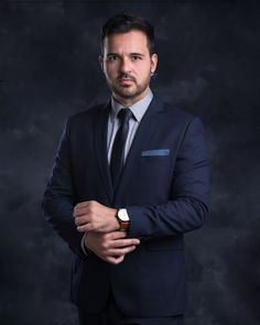 a man in a suit and tie posing for a photo with his hands folded up