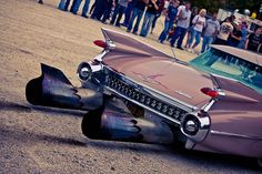 an old pink car is laying on the ground in front of a group of people