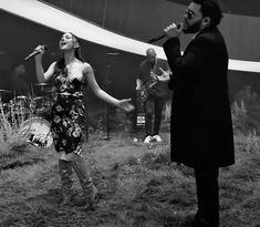 a woman singing into a microphone while standing next to a man in a suit and tie