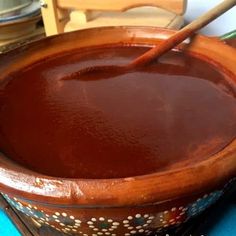 a wooden bowl filled with brown liquid on top of a blue table cloth next to a knife