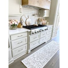 a kitchen with white cabinets and an area rug on the floor in front of the stove