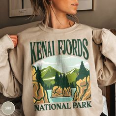 "Show off your love of nature and our nation's beautiful parks in our Kenai Fjords National Park Sweatshirt! This sweatshirt is all about embracing the great outdoors, featuring a custom design that showcases the  beauty of the Alaskan Wilderness and the stunning Kenai Fjords! Remember that once in a lifetime Alaskan Cruise or epic Alaskan adventure with this one of kind crewneck! The Gildan 18000 cotton fabric has that comfy, lived-in feel, that's like a hug every time you put it on! Now you can take a bit of Kenai with you wherever you wander! Grab one while you can, and hit the trail! * Product Highlights * Ideal for any situation, this Gildan 18000 heavy blend crewneck sweatshirt is pure comfort. Made from an extremely soft 50/50 polyester and cotton blend, this combination helps keep National Park Sweatshirt, Kenai Fjords National Park, Sweat Vintage, National Park Gifts, Kenai Fjords, Badlands National Park, Shenandoah National Park, Gifts For Campers, Bryce Canyon National Park