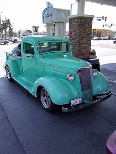 an old green truck parked in front of a gas station