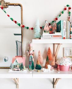 a white shelf topped with christmas trees and cupcakes covered in frosting next to a mirror