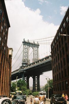 people are walking down the street in front of some tall buildings and a large bridge