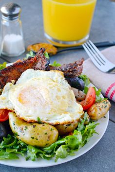 a plate with eggs, potatoes and meat on it next to a glass of orange juice