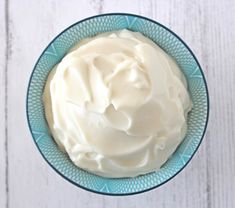 a blue bowl filled with whipped cream on top of a white wooden table next to a knife and fork