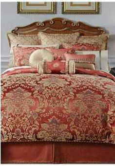 a bed with red and gold comforter in a bedroom next to a lamp on a dresser