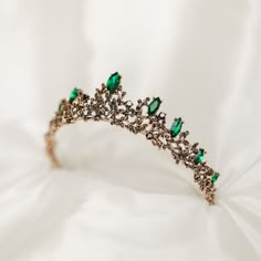 Liesel's tiara features green colored stones set into gold colored metal with dark leaf accents.  Max Height at Center: 1.5 Inches Max Length End to End: 11 Inches Head Opening: 5.5 Inches  Tiara is adjustable by carefully bending and stretching the ends apart to fit most hair styles and head sizes.  Tiara features loops on each end to secure to hair with bobby pins. Item ships from Michigan, USA. WARNING: CHOKING HAZARD This is not a toy.  This item is not intended for use by children under the age of 5 years old.  There are small pieces that could fall off and create a choking hazard.  All use of this product by any minor, child or dependent should be supervised by an adult 18 years of age or older. Emerald Green And Gold Tiara, Dark Green Tiara, Green Tiara, Emerald Tiara, Black Tiara, Flower Tiara, Gold Tiara, Tiara Hairstyles, Princess Tiara