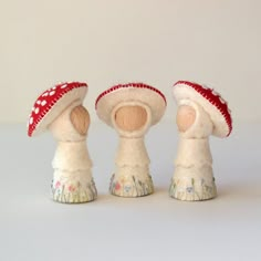 three stuffed mushrooms are sitting next to each other on a white tablecloth surface, one is wearing a red and white hat