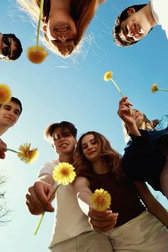 four people are standing in a circle holding dandelions and looking up at the sky