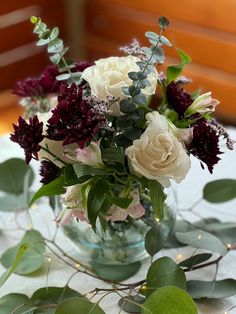 a vase filled with white and red flowers on top of a table covered in greenery