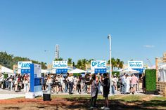 many people are standing in front of tents at an outdoor event with blue and white signs