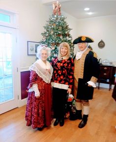 three people dressed in period costumes standing next to a christmas tree