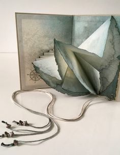 an open book with paper folded in the shape of a boat on it's side