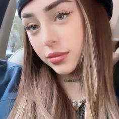 a woman with long hair wearing a hat and looking at the camera while sitting in a car