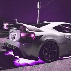 a silver sports car parked on the side of the road at night with purple lighting