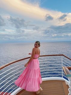 a woman in a pink dress standing on the deck of a cruise ship