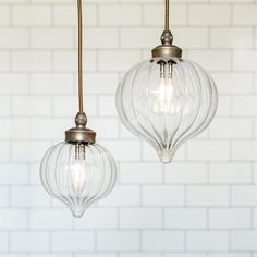 two clear glass globe lights hanging from a ceiling fixture in a white brick walled room