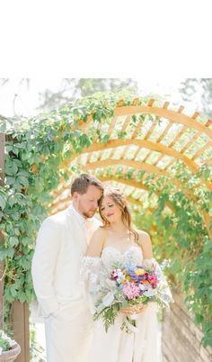 a bride and groom are standing under an arch with greenery in the background at their wedding