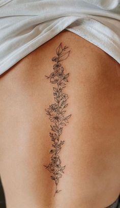 a woman's lower back tattoo with flowers on her left side ribcage