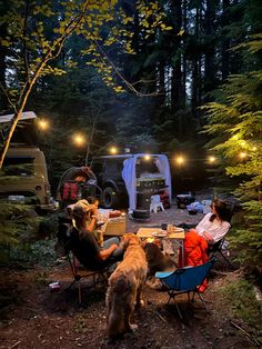 two people sitting at a table in the woods with their dogs and campers behind them