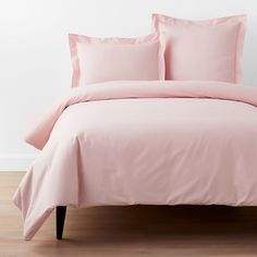 a bed with pink sheets and pillows on top of wooden flooring in front of a white wall