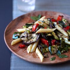 a wooden plate topped with pasta and veggies next to a glass of water