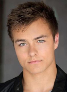 a close up of a person wearing a black jacket and blue eyes with a serious look on his face