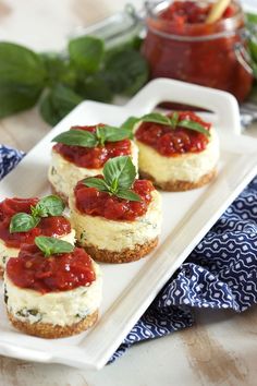 mini cheesecakes topped with fresh basil and tomato sauce on a white platter