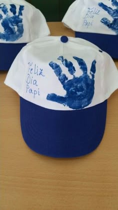 three hats with handprints on them are sitting on a table, one is blue and the other is white