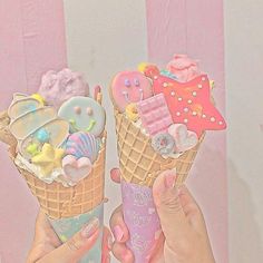 two people holding ice cream cones with different toppings on them in front of a pink background