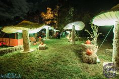 an outdoor area with hay bales and pumpkins on the ground at night time