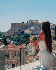 a woman sitting on top of a roof holding a wine glass in front of a cityscape