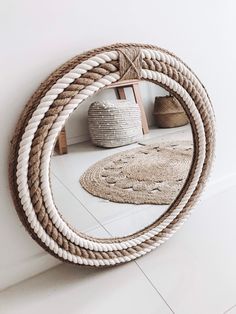 a round rope mirror sitting on top of a white floor next to a rug and basket