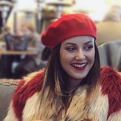 a woman wearing a red hat and fur coat sitting on a couch in a restaurant