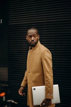 a man in a tan coat holding a white laptop