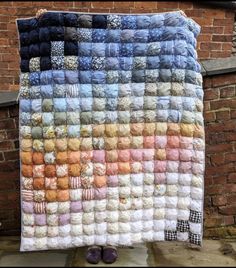 a quilt made out of several different colored yarns on a brick wall next to shoes