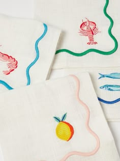 three napkins with embroidered designs on them, one has an orange and the other is a shrimp