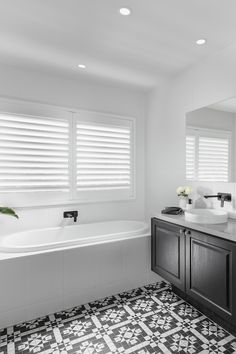 a bathroom with black and white tiles on the floor, sink, mirror and bathtub