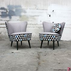 two grey chairs sitting next to each other in front of a white wall with black and blue designs on it